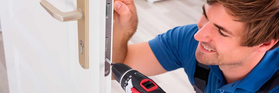 Monteur schraubt Türschloss an einer Tür fest.